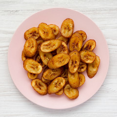 Homemade fried plantains on a pink plate over white wooden surface, top view. Flat lay, overhead, from above. Closeup.