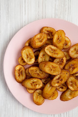 Overhead view, homemade fried plantains on a pink plate on a white wooden surface. Flat lay, overhead, from above. Close-up.