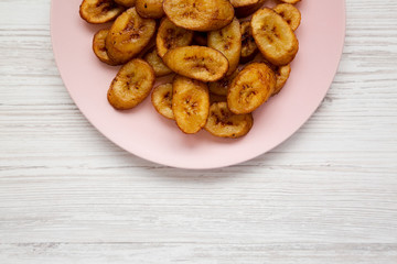Homemade fried plantains on a pink plate on a white wooden background. Flat lay, overhead, from above. Space for text.