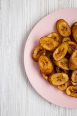 Homemade fried plantains on a pink plate on a white wooden table. Flat lay, overhead, from above. Copy space.