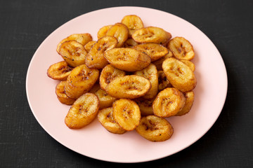 Homemade fried plantains on a pink plate on a black surface, low angle view. Close-up.