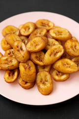 Homemade fried plantains on a pink plate on a black background,  low angle view. Close-up.