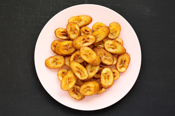 Homemade fried plantains on a pink plate on a black background, overhead view. Flat lay, from above, top view.