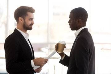 Diverse employees talking during break in office, discuss document