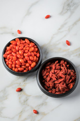 Frische und getrocknete Goji-Beeren Superfood in schwarzer Porzellan Schale auf Marmor Hintergrund