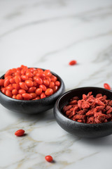 Frische und getrocknete Goji-Beeren Superfood in schwarzer Porzellan Schale auf Marmor Hintergrund