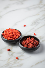 Frische und getrocknete Goji-Beeren Superfood in schwarzer Porzellan Schale auf Marmor Hintergrund