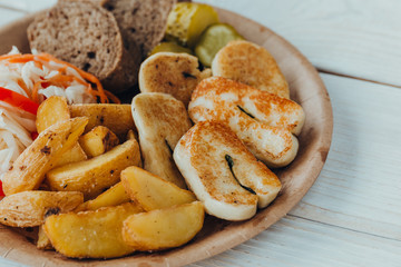 Tasty grilled fish with fried potatoes, cucumber, cabbage and woods in a paper plate on a wooden table. takeaway street food