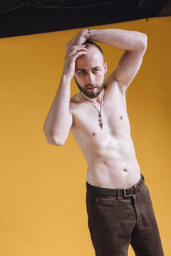 bearded man with a bare torso posing on a colored background. skinny guy after exercise and diet. emotional portrait of a student. man with a pendant around his neck