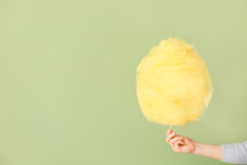 Female hand with tasty cotton candy on color background