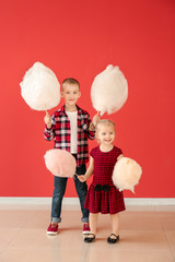 Cute little children with cotton candy against color wall
