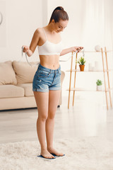 Woman with measuring tape standing on scales at home. Weight loss concept