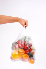 Woman’s hand holding plastic bags of vegetables on white background