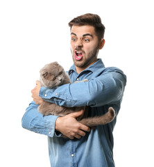 Grimacing young man with cute funny cat on white background