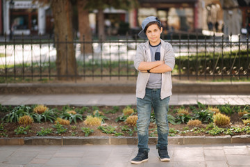 Stylish little school boy in blue cap posing outside for photo. Boy walking in the city in sping summer weather