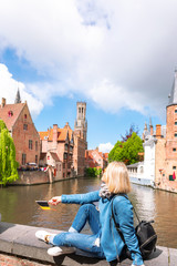 Fototapeta premium A young woman with the flag of Belgium in her hands is enjoying the view of the canals in the historical center of Bruges.