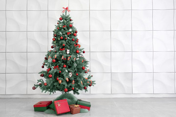 Beautiful decorated Christmas tree near white wall