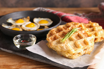 Pan with fried quail eggs and tasty squash waffles on table