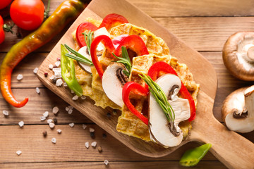 Board with tasty squash waffles and vegetables on wooden table