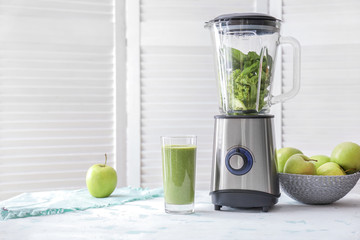 Glass of healthy smoothie and blender with ingredients on table