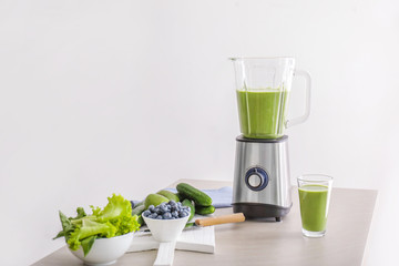 Glass of healthy smoothie, blender and ingredients on table