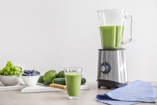 Glass of healthy smoothie, blender and ingredients on table