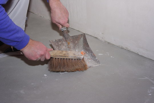 Mann reinigt Fußboden mit Handfeger und Kehrblech