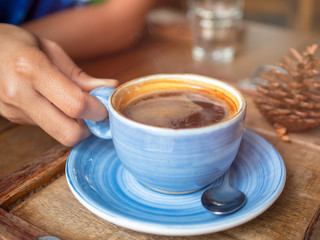 Hot American coffee is in a blue ceramic solution placed on a wooden floor table in cafe with smoke and sunlight.Coffee break in morning/ selective focus
