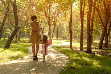 Fototapeta premium Mom holds the hand of a little girl with a balloon in the park. Close-up handshake. Happy family, mom daughter.