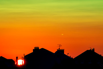 Fototapeta na wymiar Dark, clear silhouettes of the roofs of houses in the rays of the setting sun. Sunset in the city. Silhouette City landscape in the backlight of the sunset.