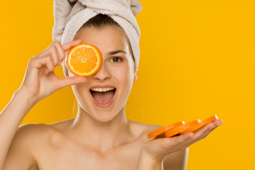 Portrait of young shirtles beautiful woman posing with  orange on yellow background