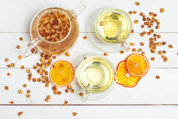 Glass kettle and cup of herbal tea on white wooden background