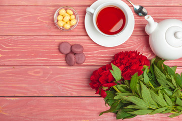 Cup of tea with sweets and flowers on wooden table