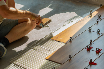 Man putting ceramic tiles on the floor in a residential home. View of a tiler's hands pressing a wood-colored tiles. Finishing a new apartment, renovation and arrangement.