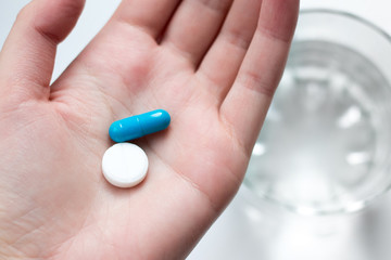 Blue and white pill capsule on the female palm. Antidepressant pills in female hand. Female hand holding a pill on the palm with a glass of water