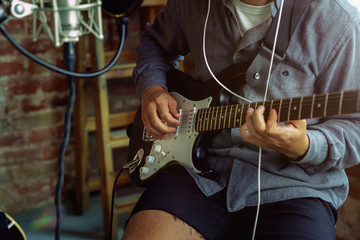 Young man in headphones recording music video blog home lesson, playing guitar or making broadcast internet tutorial while sitting in loft workplace or at home. Concept of hobby, music, art and