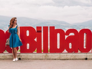 Brunette girl with long hair and a blue dress stands near the big inscription Bilbao in Bilbao on...