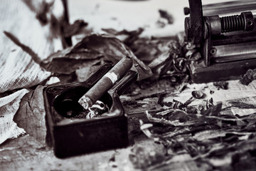close up of a Cuban cigar and a black ceramic ashtray on the wooden table whit dried and cured tobacco leaves. bw image