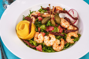Mediterranean salad. Arugula, tomatoes, shrimps, olives, olives, basil and rosemary, dressed with olive oil and balsamic sauce, decorated with lemon and chili pepper