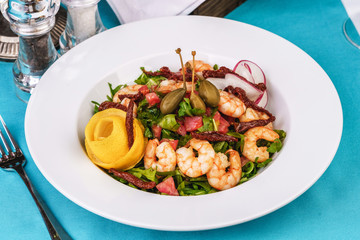 Mediterranean salad. Arugula, tomatoes, shrimps, olives, olives, basil and rosemary, dressed with olive oil and balsamic sauce, decorated with lemon and chili pepper