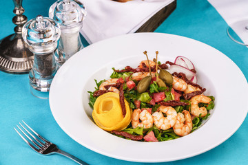 Mediterranean salad. Arugula, tomatoes, shrimps, olives, olives, basil and rosemary, dressed with olive oil and balsamic sauce, decorated with lemon and chili pepper