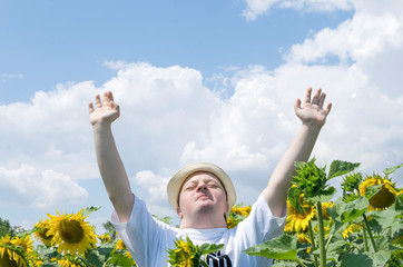 Happy and grateful young man with open arms in the sunflower field