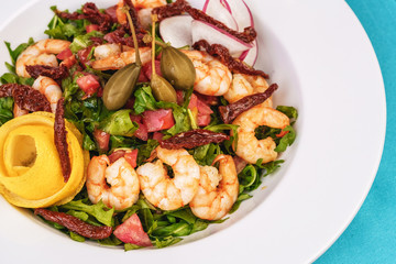 Mediterranean salad. Arugula, tomatoes, shrimps, olives, olives, basil and rosemary, dressed with olive oil and balsamic sauce, decorated with lemon and chili pepper
