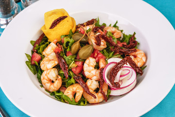Mediterranean salad. Arugula, tomatoes, shrimps, olives, olives, basil and rosemary, dressed with olive oil and balsamic sauce, decorated with lemon and chili pepper