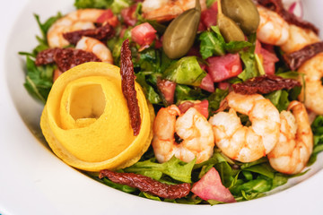 Mediterranean salad. Arugula, tomatoes, shrimps, olives, olives, basil and rosemary, dressed with olive oil and balsamic sauce, decorated with lemon and chili pepper