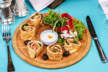 Mediterranean snack. Rolls with salmon, greens, cucumber and vegetables with cream sauce