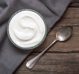 White yogurt in glass bowl on old wooden desk with old rustic spoon.