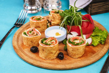 Mediterranean snack. Rolls with salmon, greens, cucumber and vegetables with cream sauce