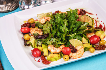 Mediterranean salad with grilled shrimps, cherry tomatoes, arugula, greens, avocado, lime, olives, balsamic sauce