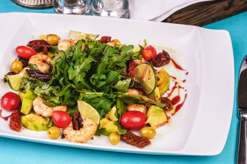 Mediterranean salad with grilled shrimps, cherry tomatoes, arugula, greens, avocado, lime, olives, balsamic sauce